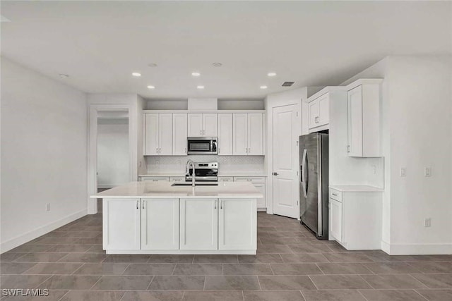 kitchen featuring stainless steel appliances, an island with sink, tasteful backsplash, and white cabinetry