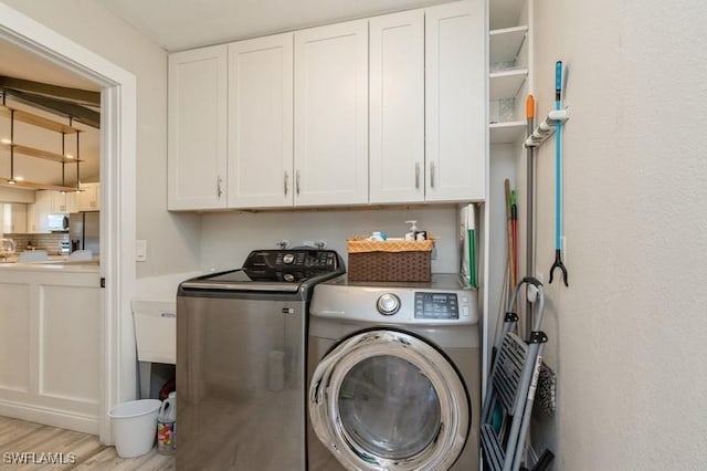 clothes washing area featuring cabinets, light wood-type flooring, and washer and clothes dryer