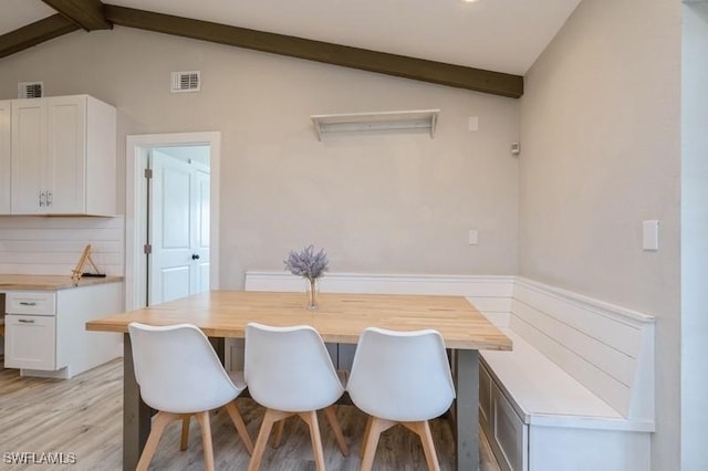 dining space with light hardwood / wood-style flooring and lofted ceiling with beams