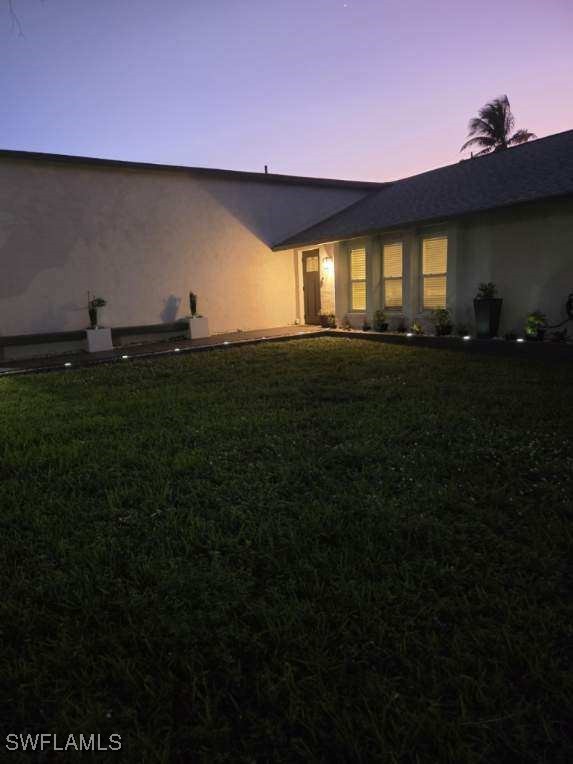 back house at dusk featuring a lawn