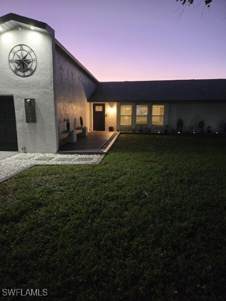 back house at dusk featuring a garage and a yard