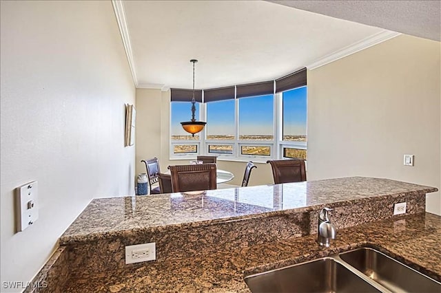 kitchen featuring dark stone countertops, ornamental molding, sink, and hanging light fixtures