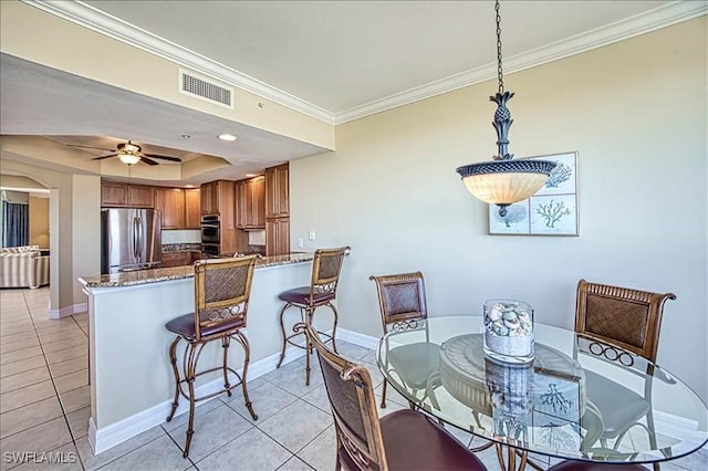 tiled dining space with ceiling fan, a raised ceiling, and crown molding