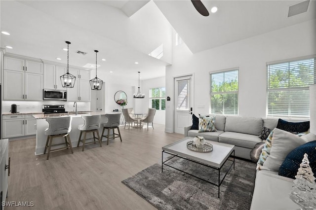 living room with ceiling fan, sink, high vaulted ceiling, and light hardwood / wood-style flooring