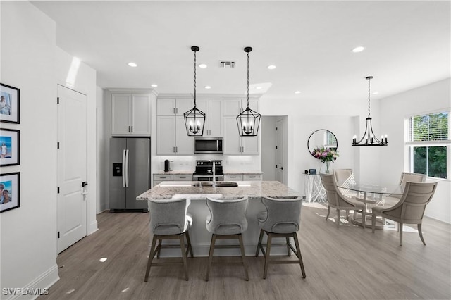 kitchen with a center island with sink, light hardwood / wood-style flooring, light stone countertops, a kitchen bar, and stainless steel appliances