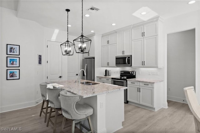 kitchen with light stone counters, an island with sink, a breakfast bar, white cabinets, and appliances with stainless steel finishes