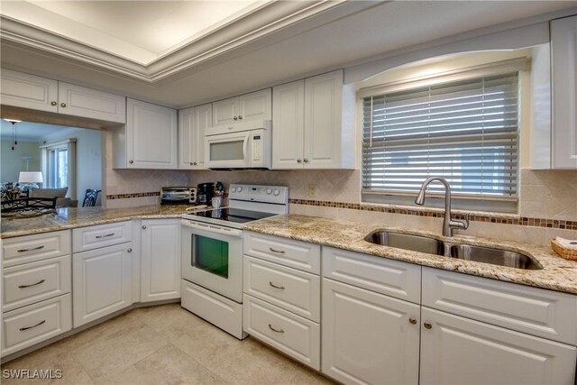 kitchen with white appliances, a sink, white cabinetry, decorative backsplash, and a tray ceiling