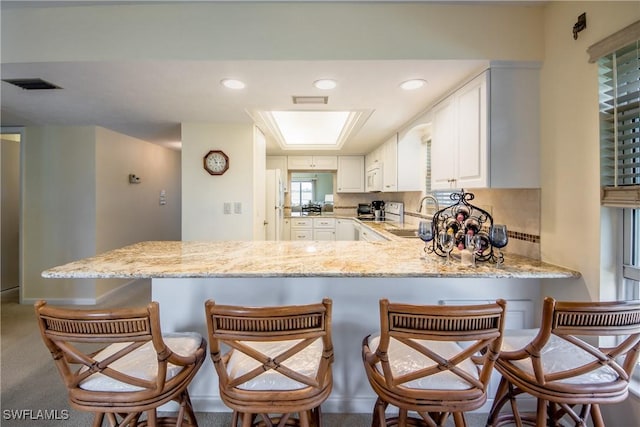 kitchen with visible vents, white cabinets, a kitchen breakfast bar, a peninsula, and a sink