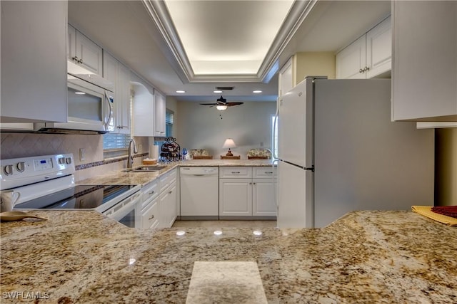 kitchen with a raised ceiling, a sink, white appliances, white cabinetry, and light stone counters