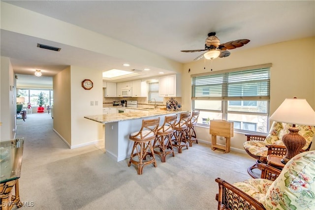 kitchen with light stone counters, a peninsula, white appliances, white cabinetry, and a kitchen bar