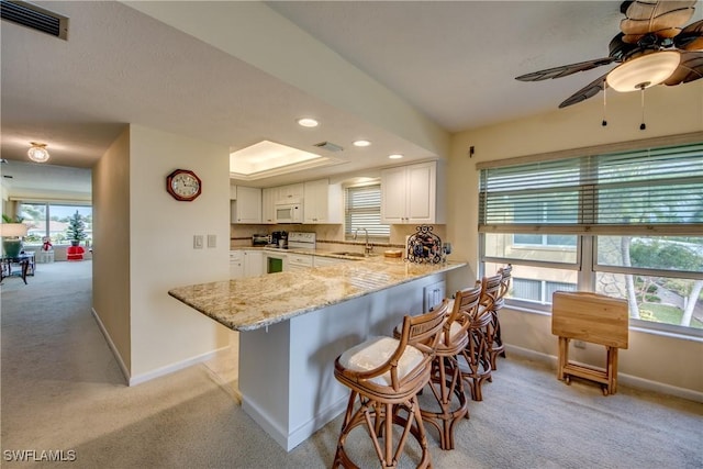 kitchen featuring baseboards, a sink, ceiling fan, white appliances, and light carpet