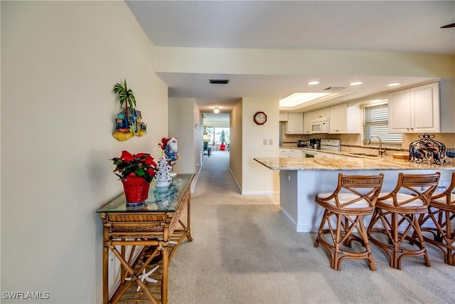 kitchen with white appliances, a breakfast bar, a peninsula, white cabinetry, and a sink