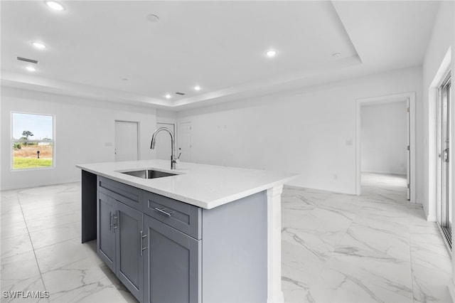 kitchen with a center island with sink, a raised ceiling, gray cabinetry, and sink