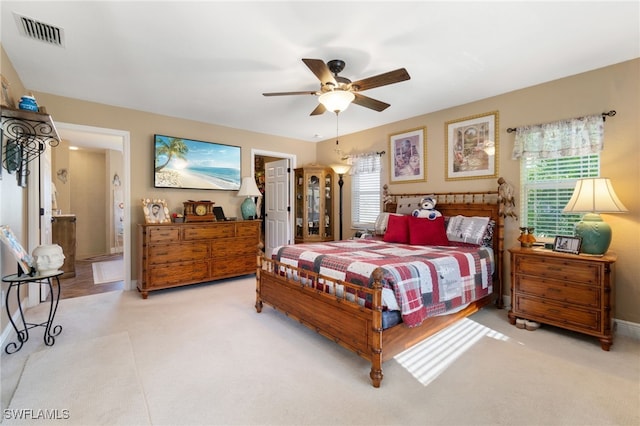 bedroom with multiple windows, ceiling fan, ensuite bath, and light colored carpet