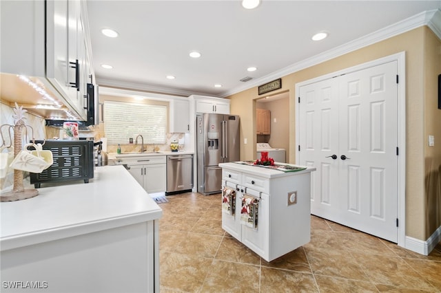 kitchen with white cabinetry, washer / clothes dryer, appliances with stainless steel finishes, a kitchen island, and ornamental molding