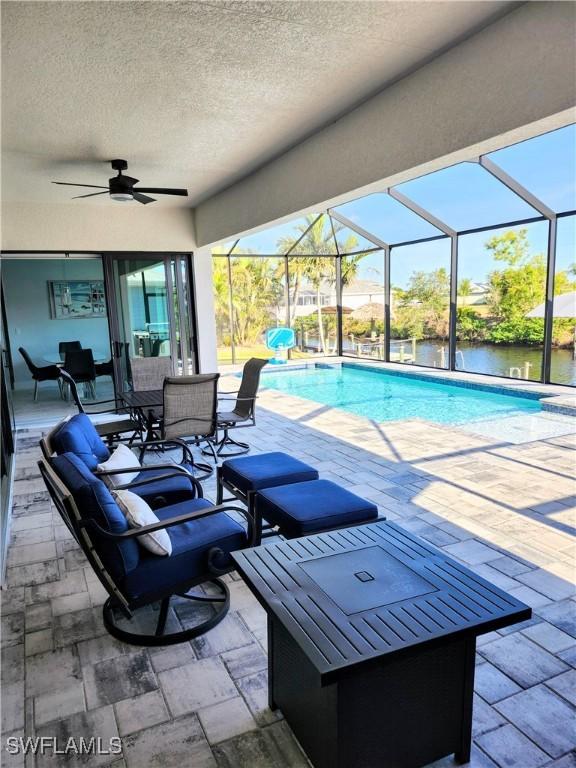 view of swimming pool featuring a patio area, ceiling fan, a water view, and glass enclosure