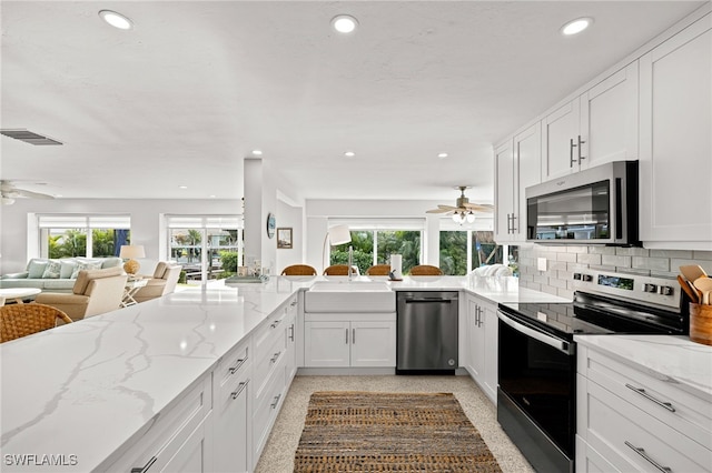 kitchen featuring kitchen peninsula, light stone countertops, stainless steel appliances, sink, and white cabinets