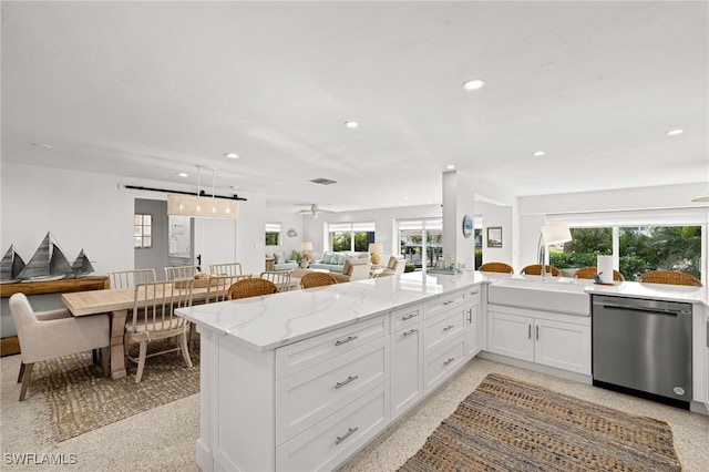 kitchen with stainless steel dishwasher, light stone counters, white cabinetry, and a wealth of natural light