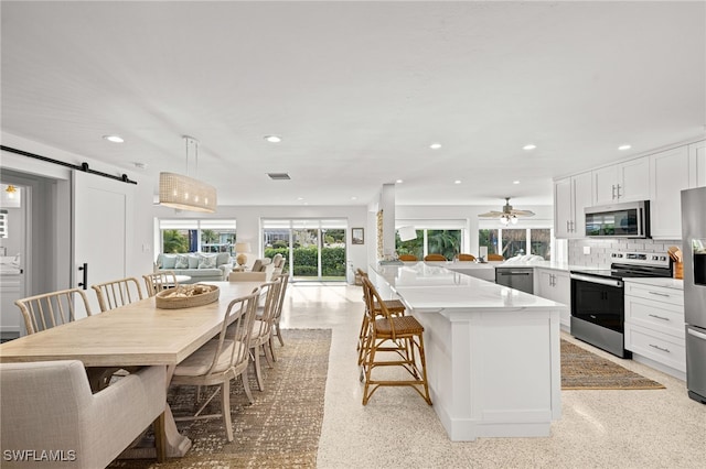 kitchen with white cabinets, a barn door, stainless steel appliances, and hanging light fixtures