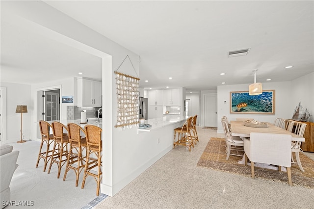 kitchen featuring stainless steel fridge with ice dispenser, decorative backsplash, white cabinetry, and pendant lighting