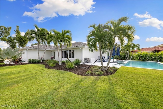 rear view of property with a patio area, a lawn, an outdoor pool, and stucco siding