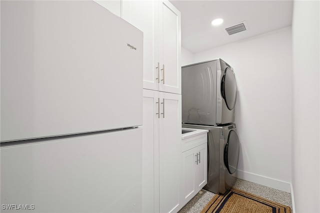 washroom featuring stacked washer / drying machine and cabinets