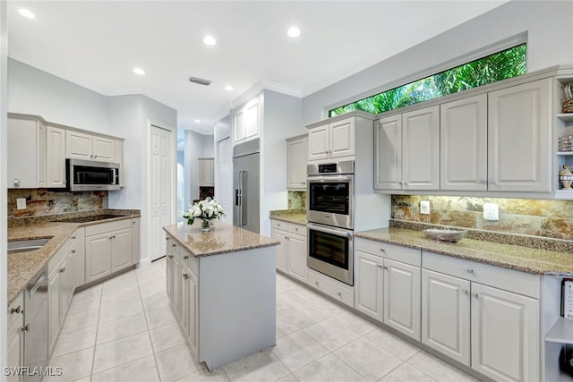 kitchen featuring decorative backsplash, light stone counters, ornamental molding, stainless steel appliances, and white cabinets