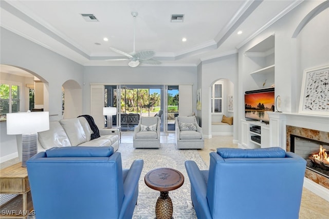 tiled living room with a high end fireplace, a wealth of natural light, crown molding, and ceiling fan