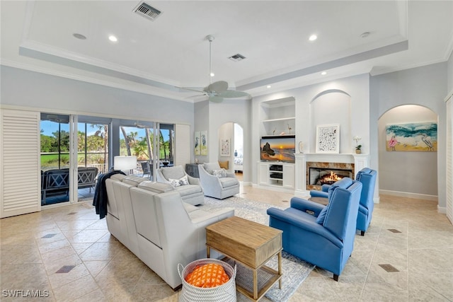 living room featuring ceiling fan, built in features, crown molding, a tray ceiling, and light tile patterned floors