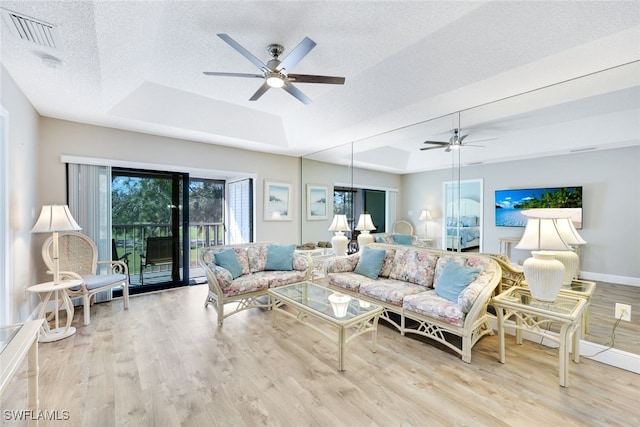 living room with ceiling fan, a raised ceiling, light wood-type flooring, and a textured ceiling