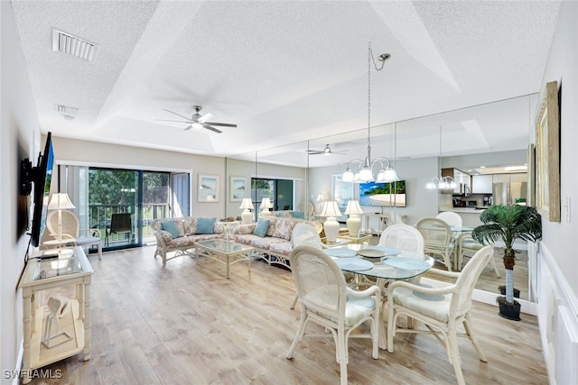 dining room featuring a textured ceiling, ceiling fan with notable chandelier, light hardwood / wood-style floors, and a tray ceiling