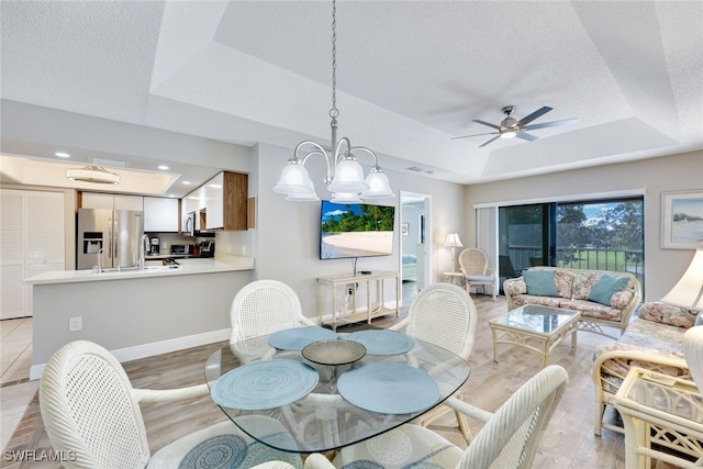 dining area featuring ceiling fan with notable chandelier, light hardwood / wood-style floors, a raised ceiling, and a textured ceiling