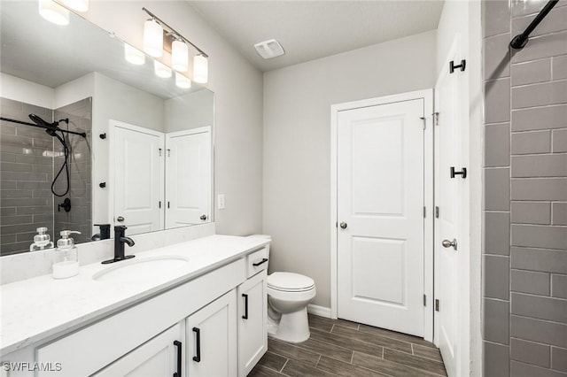 bathroom featuring a tile shower, vanity, and toilet