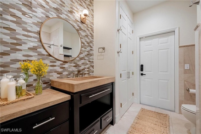 bathroom with vanity, backsplash, tile patterned floors, toilet, and tile walls