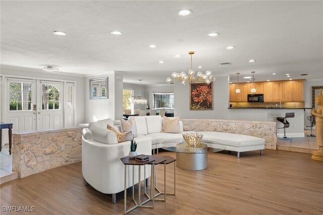 living room with a notable chandelier, ornamental molding, and light wood-type flooring