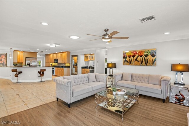 living room featuring ceiling fan, ornamental molding, and light hardwood / wood-style floors