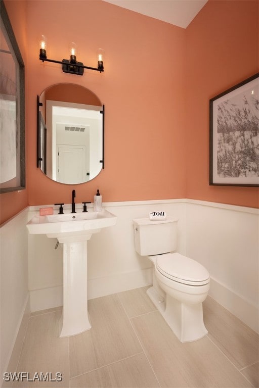 half bath featuring toilet, tile patterned flooring, visible vents, and baseboards