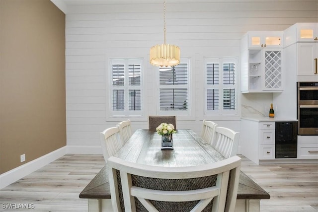 dining space with a chandelier, light hardwood / wood-style flooring, beverage cooler, and wooden walls