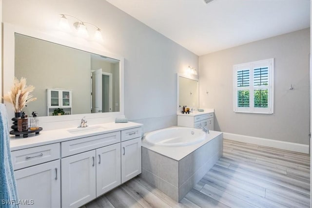 bathroom featuring wood-type flooring, vanity, and a relaxing tiled tub