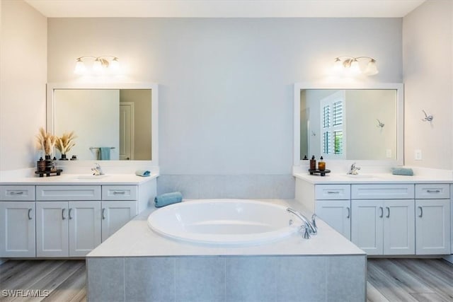 bathroom featuring tiled tub, vanity, and wood-type flooring