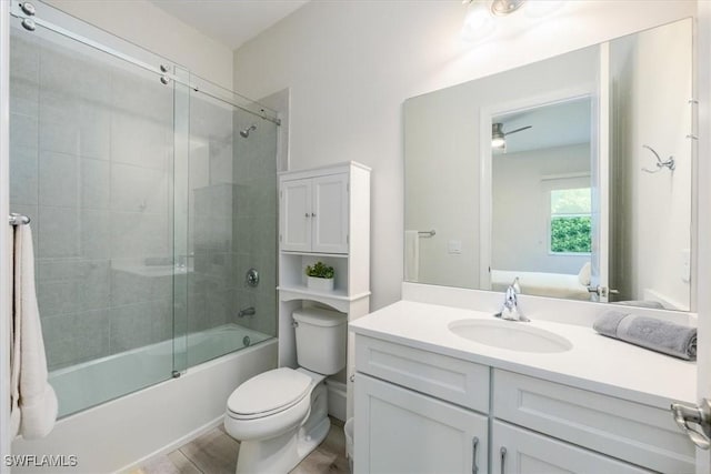 full bathroom featuring combined bath / shower with glass door, vanity, ceiling fan, wood-type flooring, and toilet