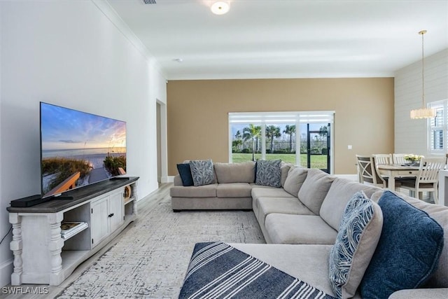 living room featuring a notable chandelier, plenty of natural light, light wood-type flooring, and crown molding