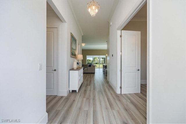 hallway featuring light wood-type flooring, ornamental molding, and a chandelier