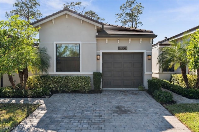 view of front facade featuring a garage, decorative driveway, a tiled roof, and stucco siding