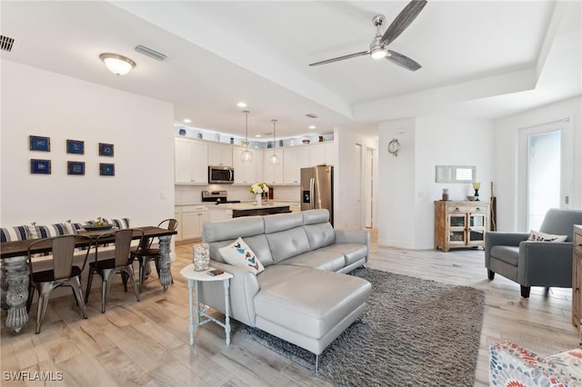 living room featuring a raised ceiling, ceiling fan, and light hardwood / wood-style floors