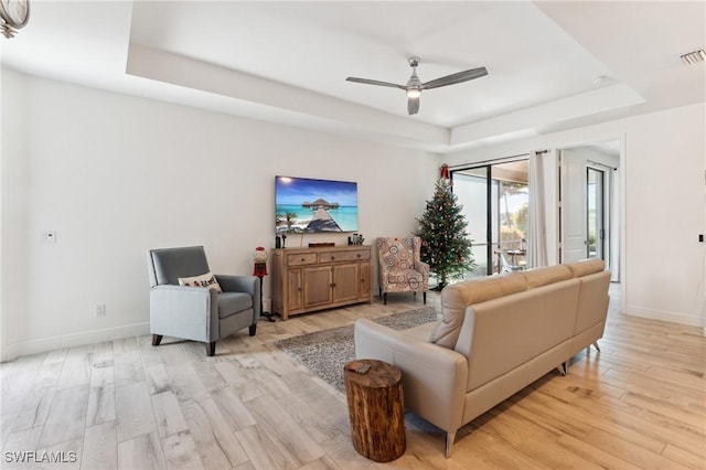 living room featuring a raised ceiling, ceiling fan, and light hardwood / wood-style floors