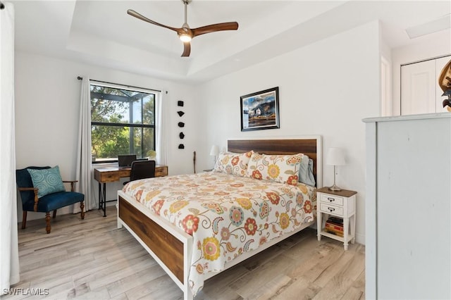 bedroom with light wood-style floors, ceiling fan, and a tray ceiling