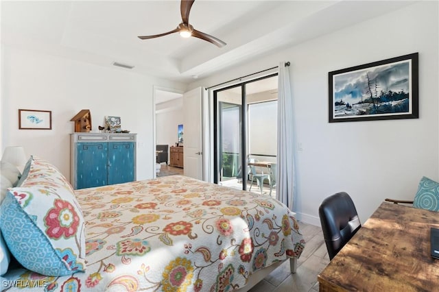 bedroom featuring access to exterior, a tray ceiling, ceiling fan, and light wood-type flooring