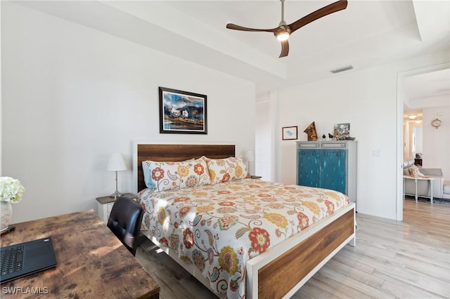 bedroom with ceiling fan, a raised ceiling, and light wood-type flooring