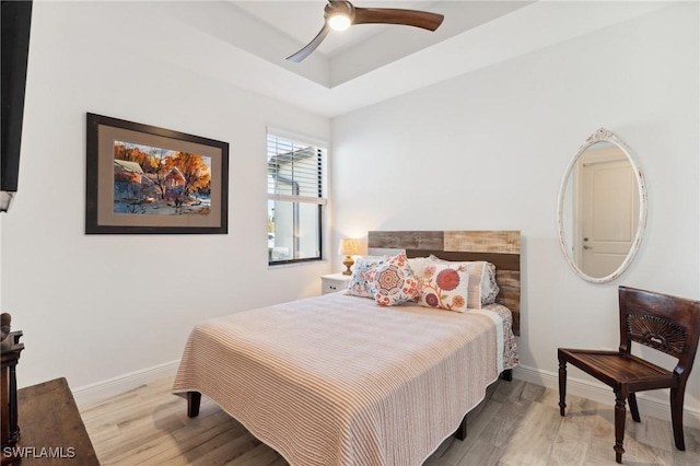 bedroom featuring light hardwood / wood-style floors, a raised ceiling, and ceiling fan